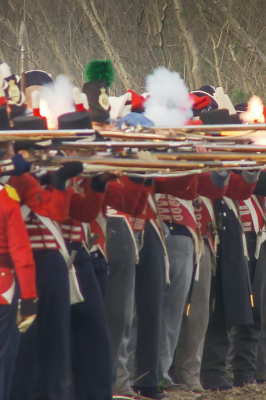 A line of British Army red coat reenactors fire their muskets