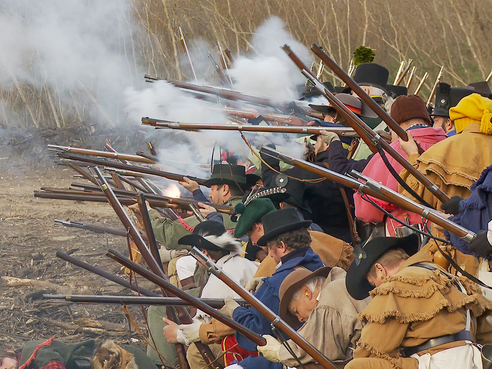 dozens of military reenactors dressed in the period uniforms of volunteers and militia fire muskets in this battle reenactment