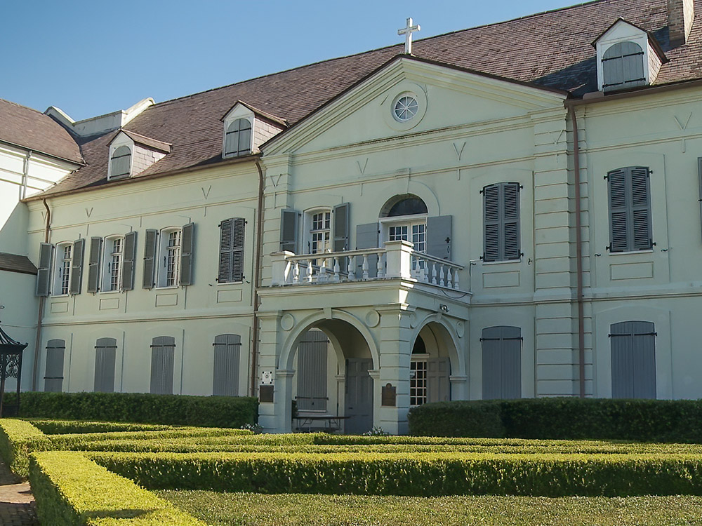 exterior of the 3-story Old Ursuline Convent in New Orleans showing cross above front entrance and garden