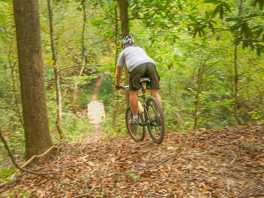 mountain biker descends steep portion of trail toward a wooden creek crossing while biking the beast in St. Francisville Louisiana