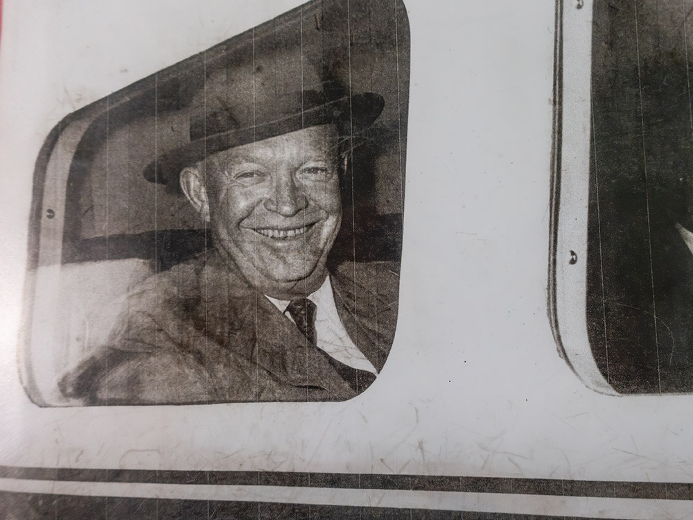 President Eisenhower wearing suit and hat looks out of window of small Air Force One aircraft in 1950s