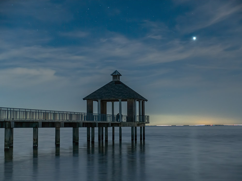 long pier and pavillion over lake Pontchartrain with conjunction of jupiter and saturn appearing as bright star above still lake