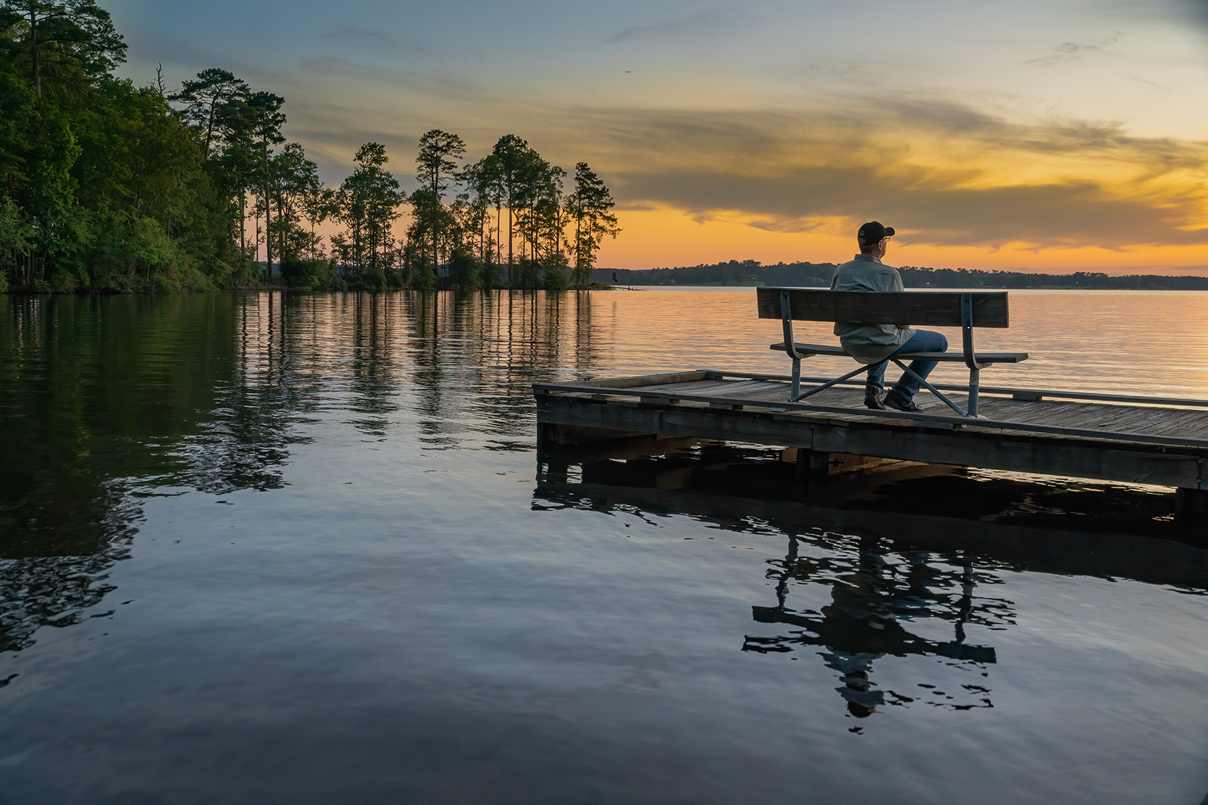sunset at Louisiana State Park with calm lake orange sky and silhouette of man setting on bench