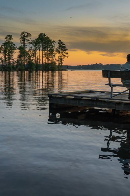 man sitting on dock in peaceful setting on Caney Lake at sunset