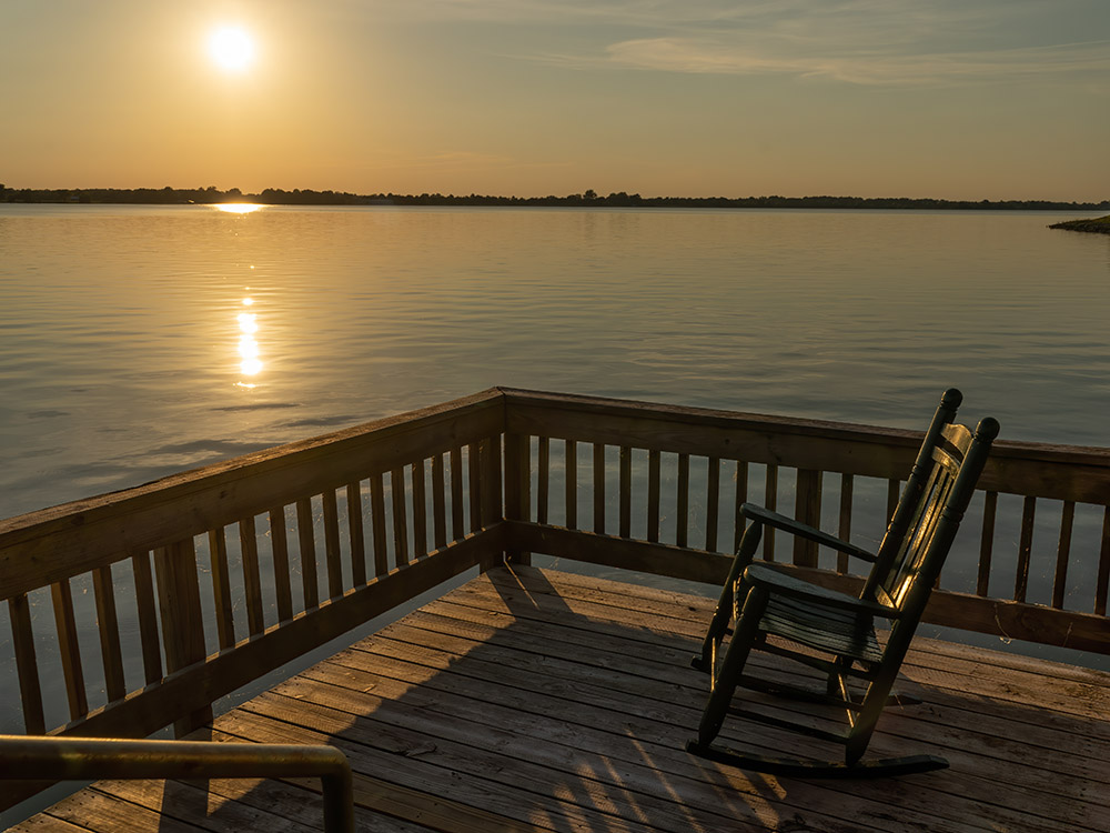 view from cabin deck of wooden rocking chair and golden sunset over Poverty Point Reservoir State Park
