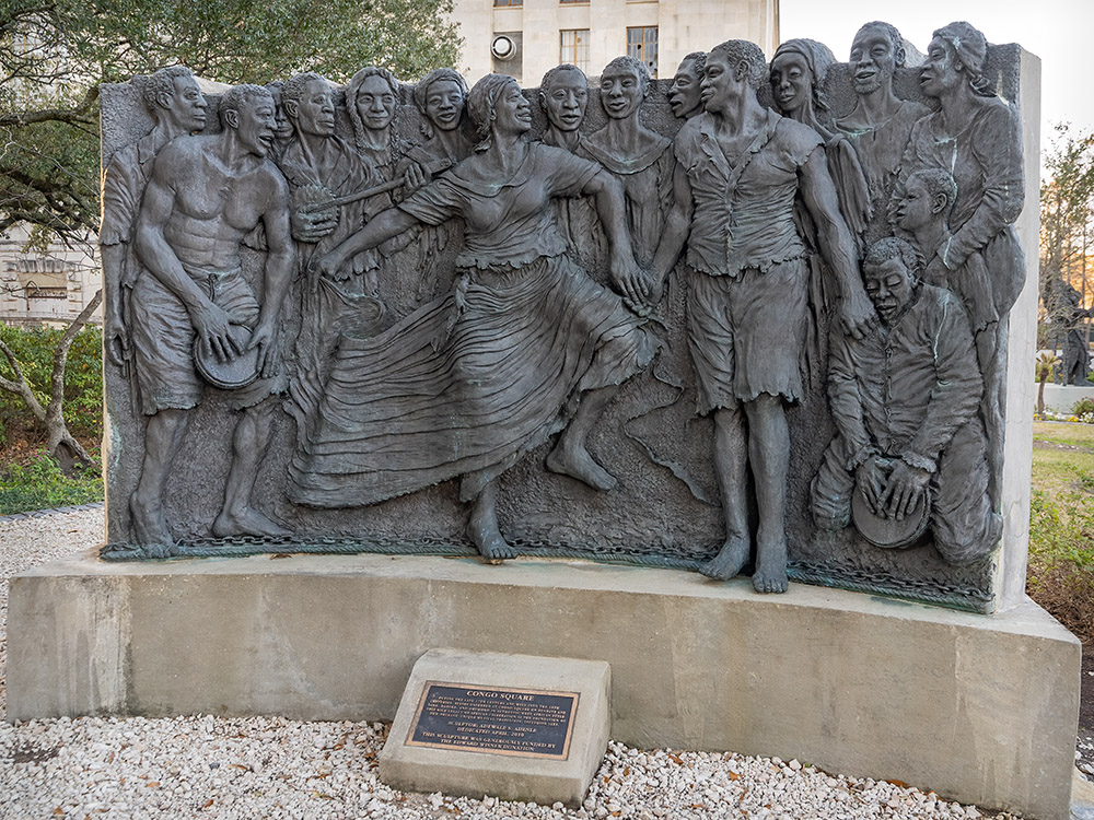 bronze scene from historic picture of enslaved Africans gathering, playing drums and dancing in Congo Square