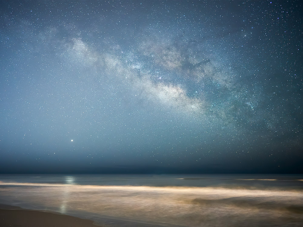 milky way above beach at gulf shore with Jupiter reflecting in the surg