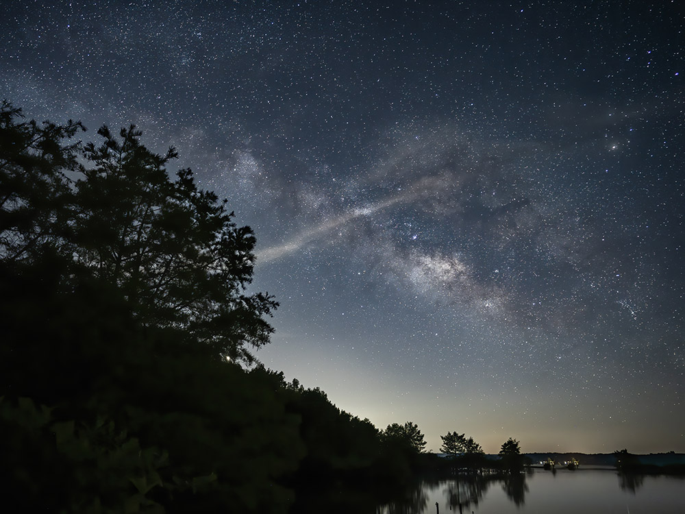 milky way mixes with clouds above lake and trees