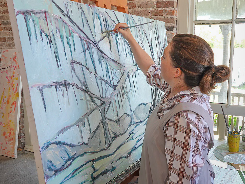 artist Leslie Ratcliff brushes paint on picture of tree in studio in St. Joseph Louisiana