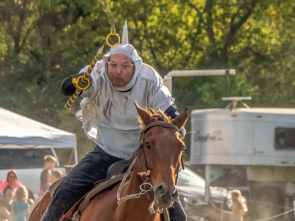 costumed rider on horseback takes aim at small yellow ring in tournament