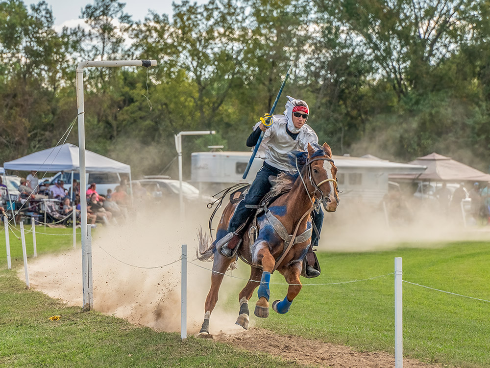 horse kicks up dust as rider with lance catches rings at le Tournoi