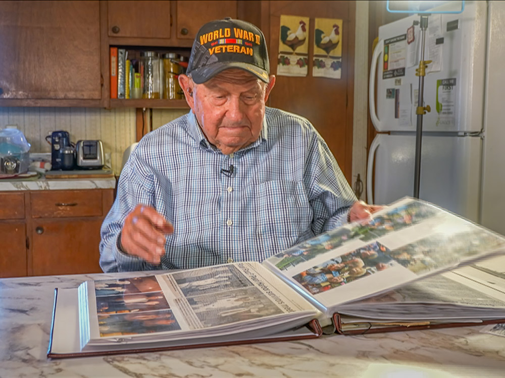elderly man in veterans cap looks at pearl harbor scrapbook