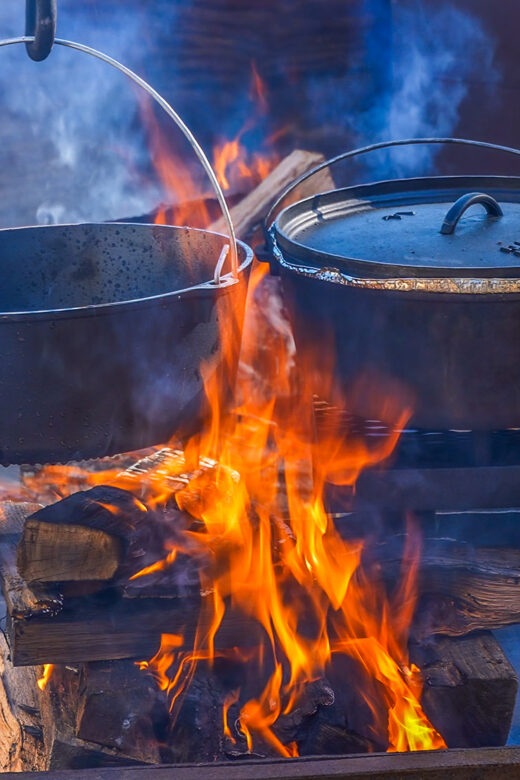 2 black cast iron pots dutch oven over log flames