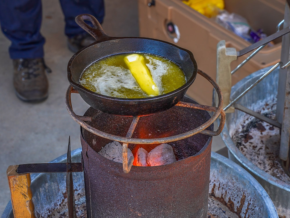 stick of butter melting in black pan over hot coals