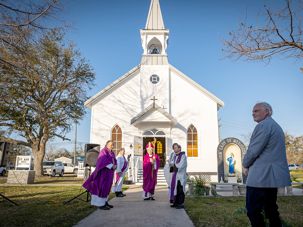 atchbishop and other clerics in purple robes stand in front of white church with steeple