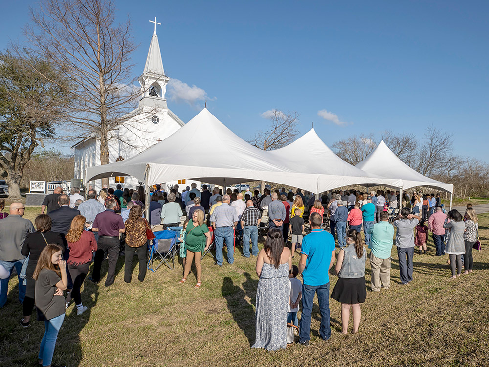 large crowd and white tents in front of white church with steeple
