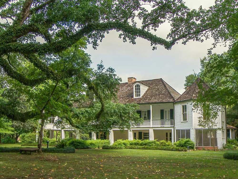 white two story french colonial plantation home with large oak trees Melrose