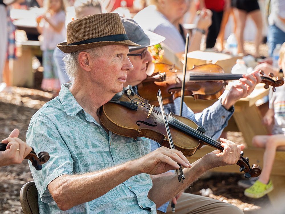 man in blue shirt and hat plays fiddle with others at Lafayette Farmers Market