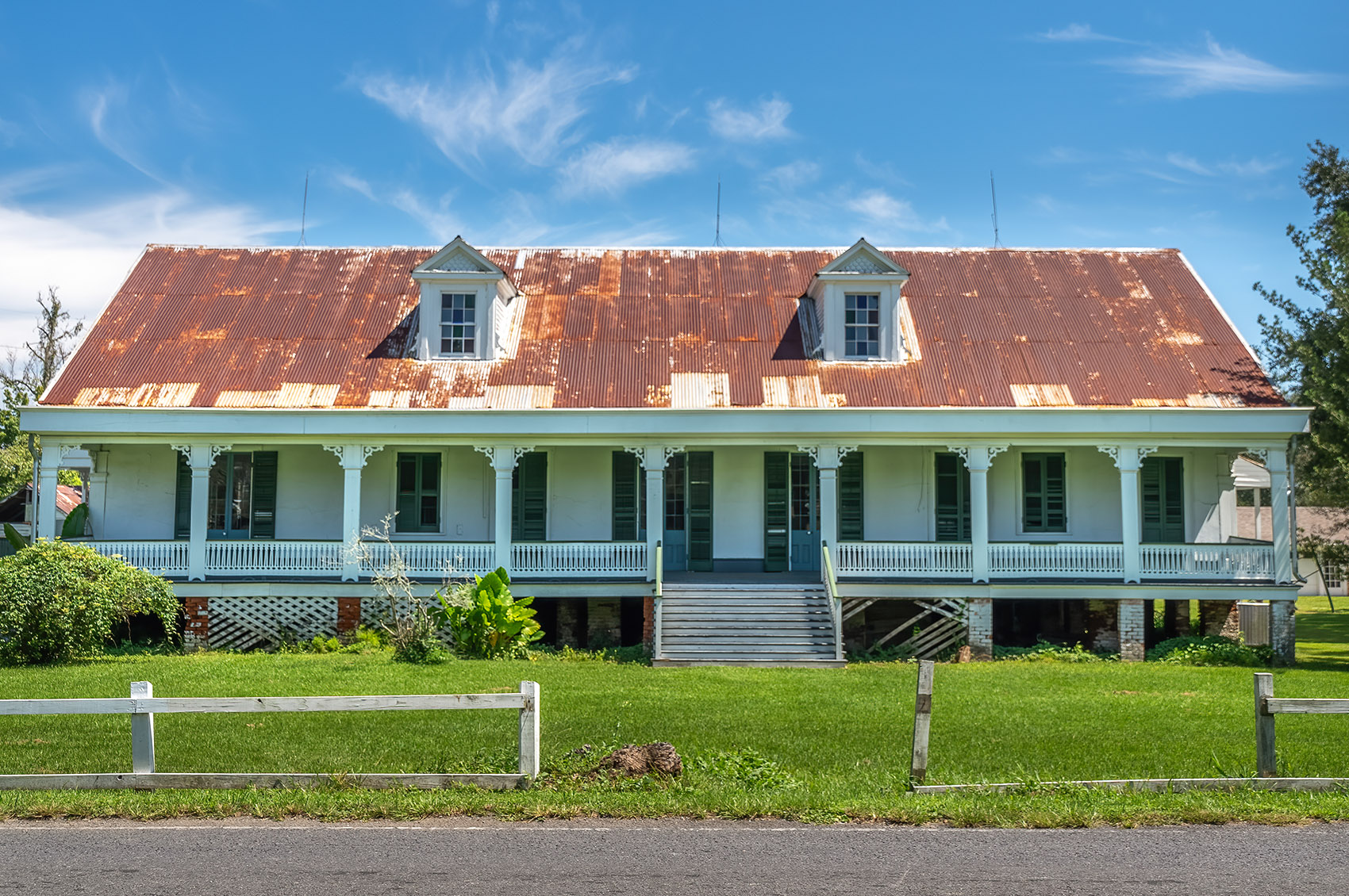 1811 Kid Ory white plantation style house with gallery dormers and rusted metal roof under blue sky