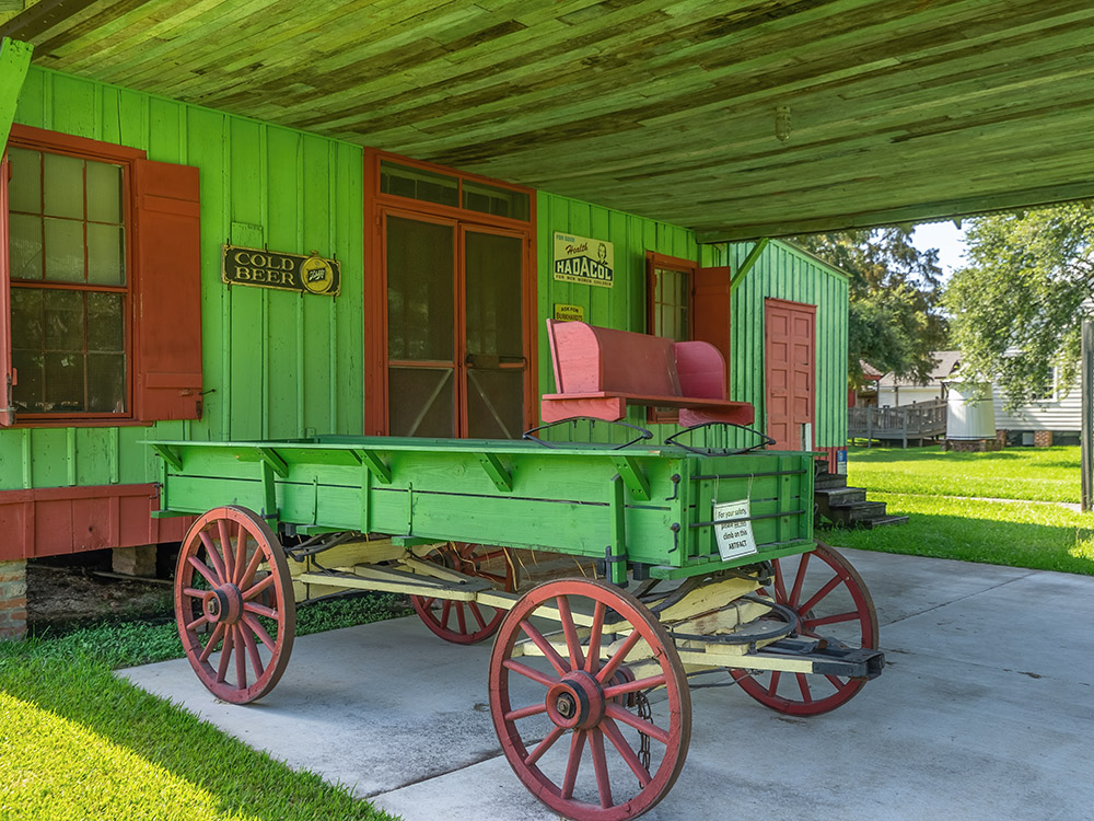 Green horse-drawn wagon in front of old general store at West Baton Rouge Museum
