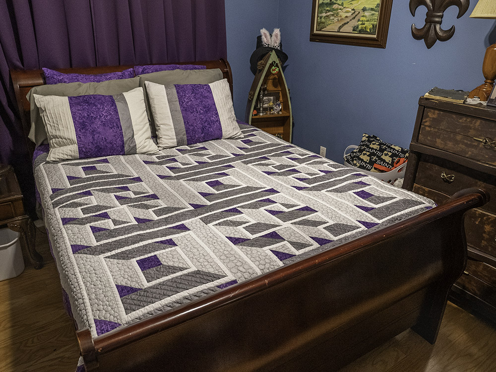 purple and gray squares on quilt on bed with purple drapes and blue bedroom wall