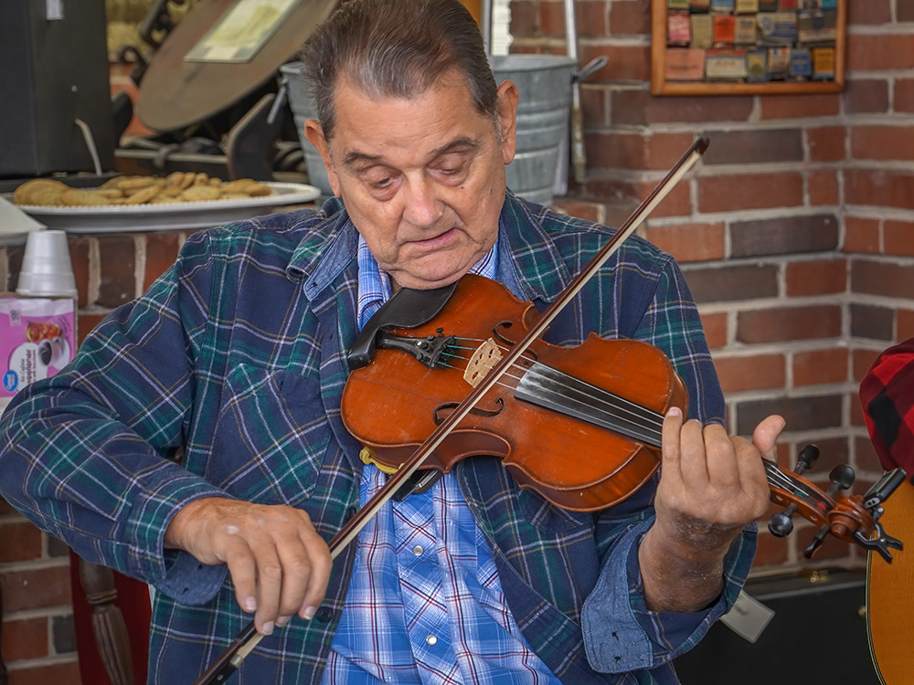 man in plaid blue shirt plays fiddle at bluegrass jam