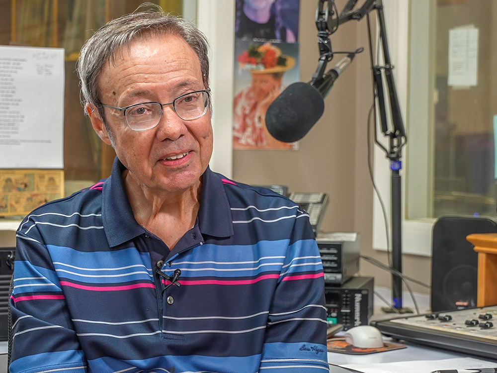 Mark Layne man wearing glasses and blue striped shirt sitting near microphone in radio studio