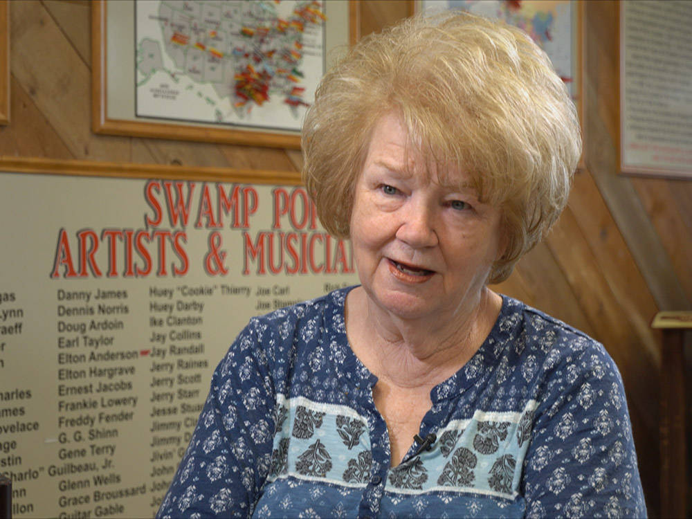 woman with blond hair and blue patterned blouse in front of swamp pop museum display