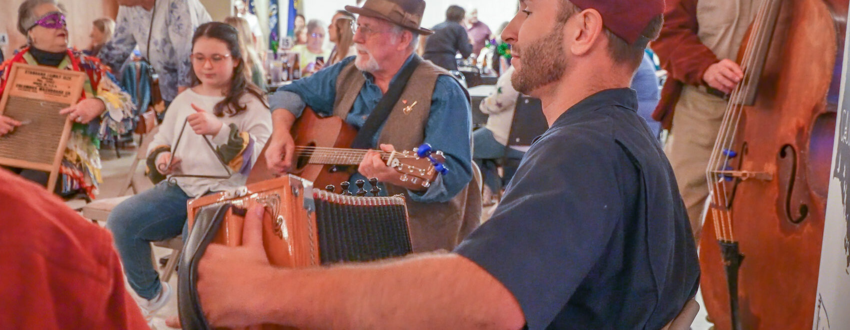 man in blue shirt and red cap playing accordion and man in blue shirt and hat playing guitar at jam session