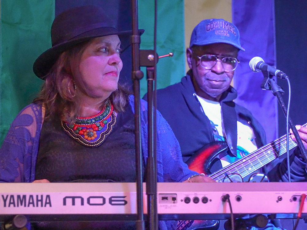 woman wearing hat plays keyboard and men wearing cap plays bass guitar on stage at Blue Monday in Lafayette