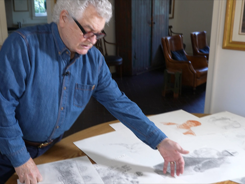 artist Henry Casselli points to sketches of horses and riders on a table