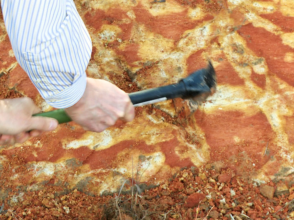 hammer being used to scrape earth to reveal clay fractures at site of Louisiana meteor crater