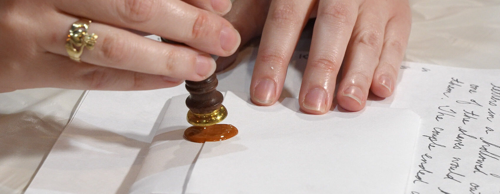 woman's hands adding wax and seal to a folded letter