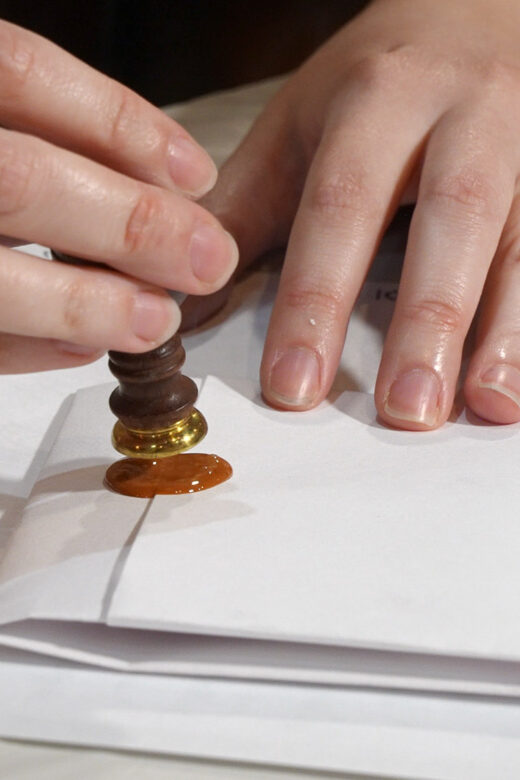 woman's hands adding wax and seal to a folded letter