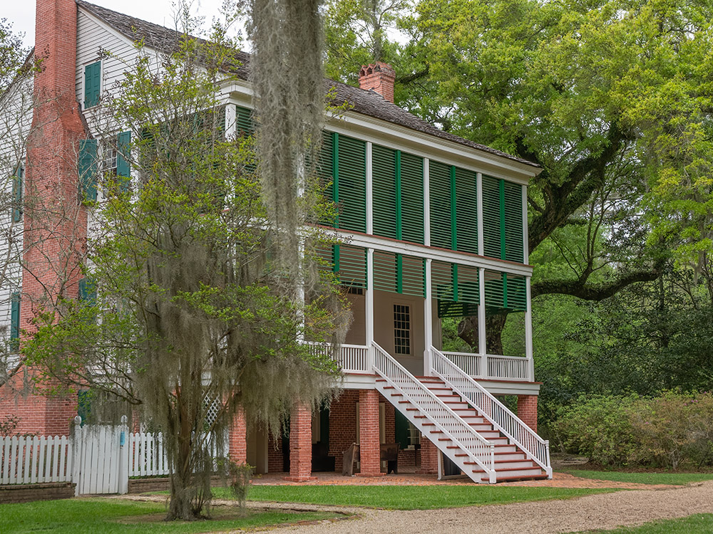 3 story white plantation home with green shutters on porch surrounded by moss draped oak trees