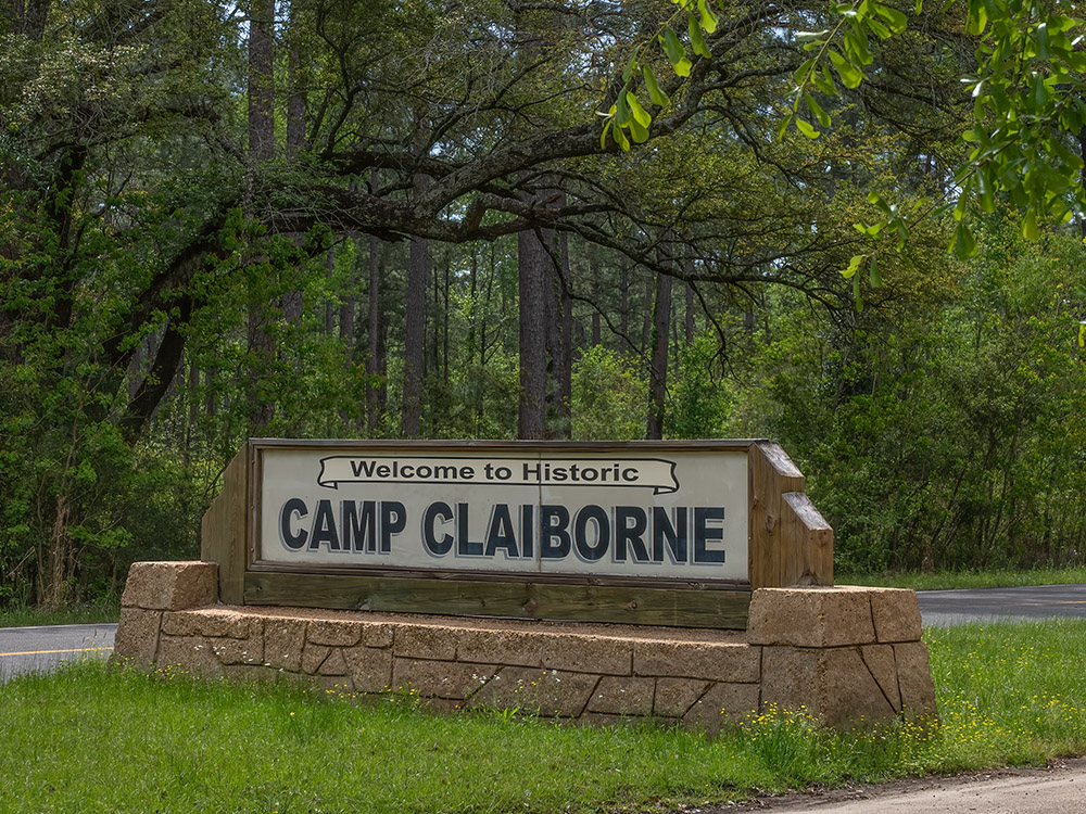 large stone and wood sign for Camp Claiborne along roadside in forest