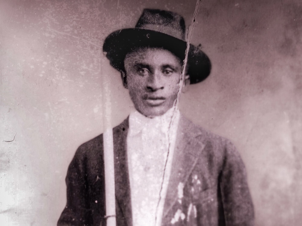 old black and white photograph of man Amede Ardoin wearing dark coat, white shirt and dark hat.
