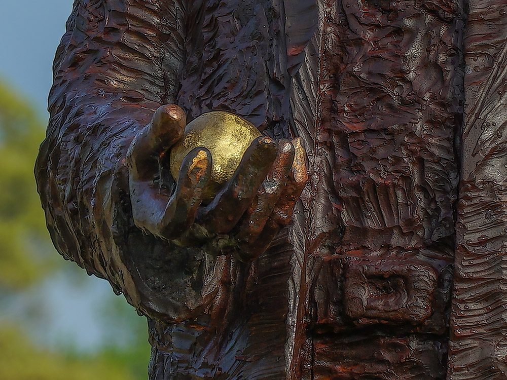 bronze statue of man's hand holding golden lemon