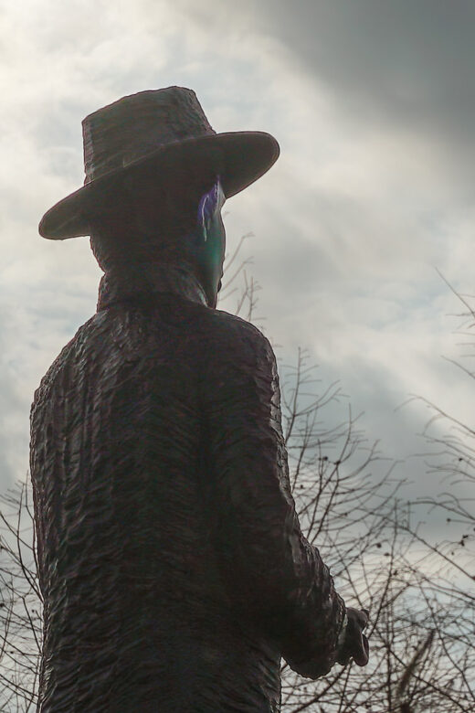 statue of man wearing had in silhouette with bare trees