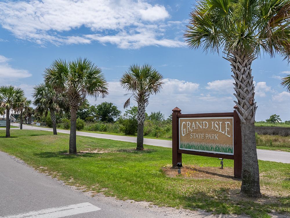 grand isle state park entrance sign with palm trees under blue sky