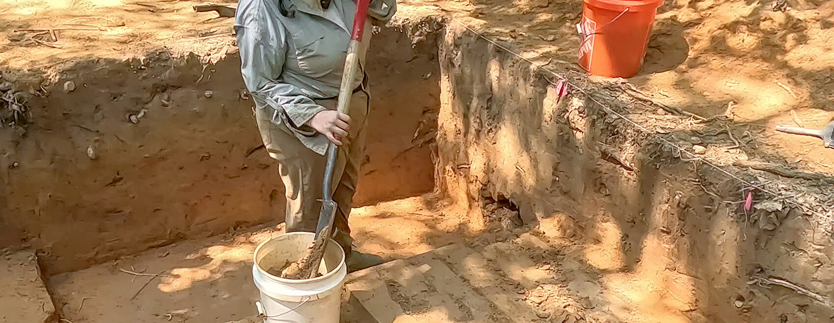 woman wearing hat with shovel and bucket in archealogy dig