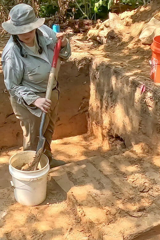 woman wearing hat with shovel and bucket in archealogy dig