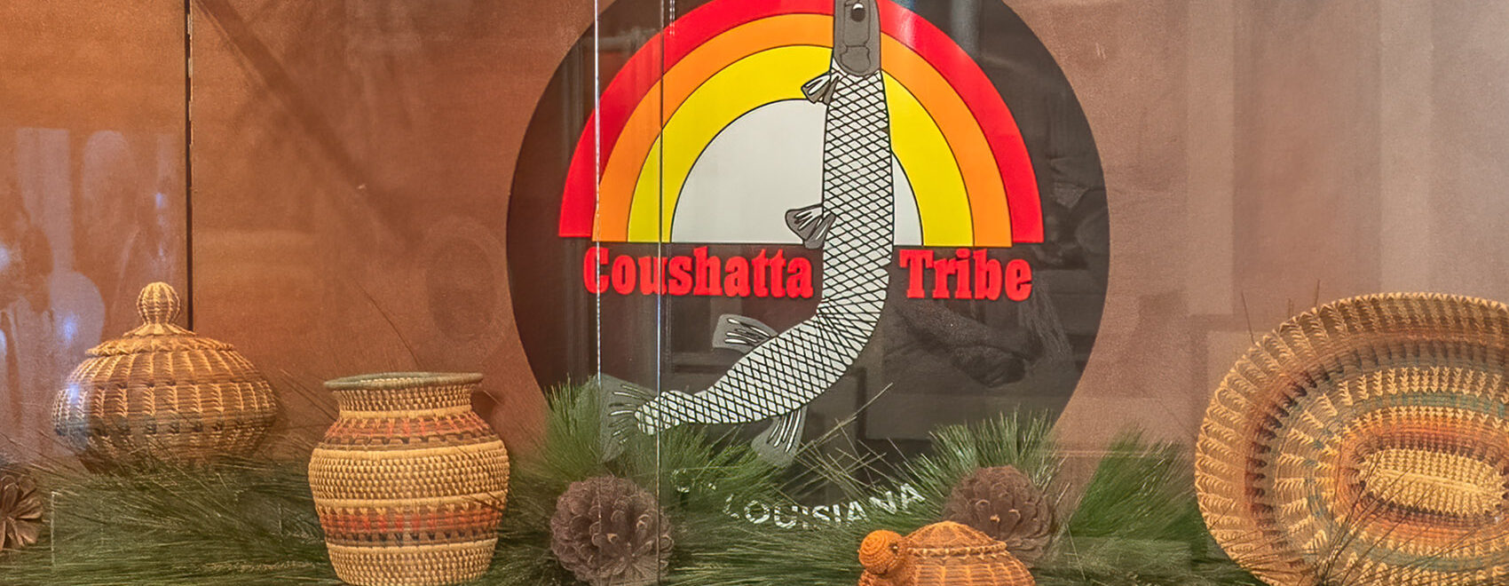 brown red orange and yellow round seal of Coushatta Tribe with garfish and baskets