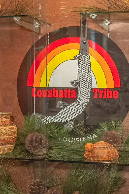 brown red orange and yellow round seal of Coushatta Tribe with garfish and baskets