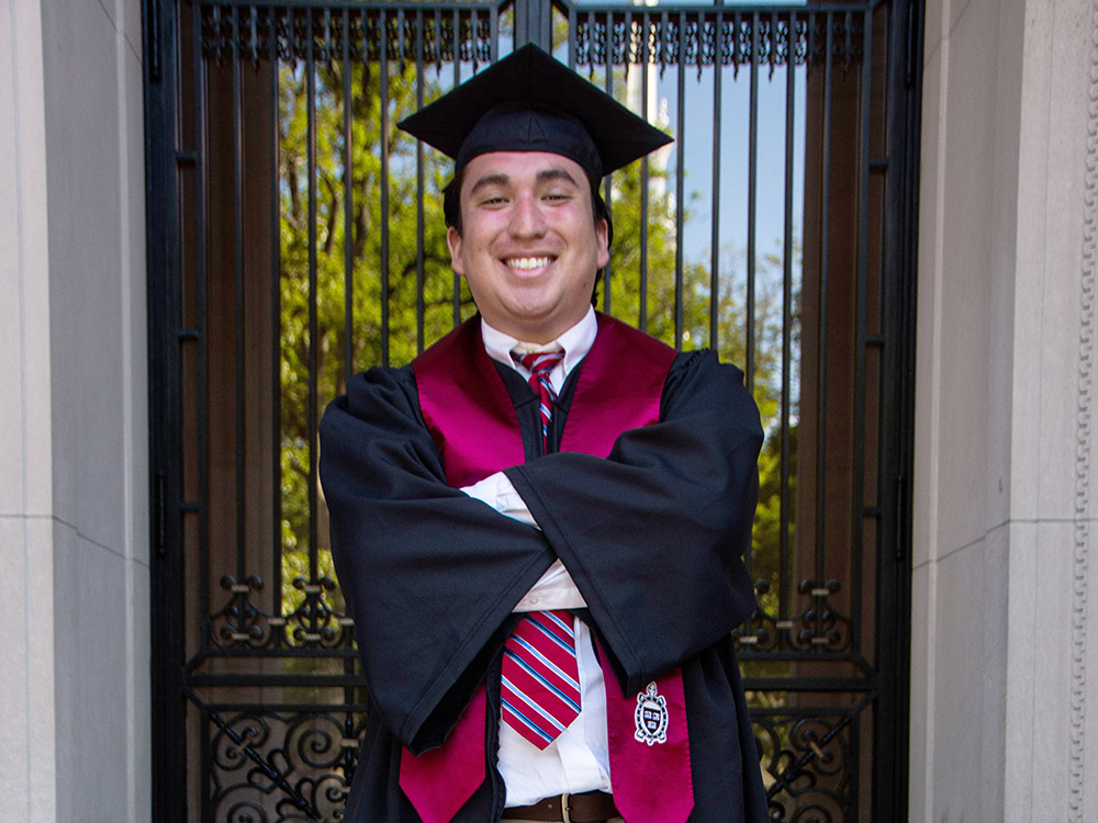 male student in Harvard cap and gown smiling at graduation