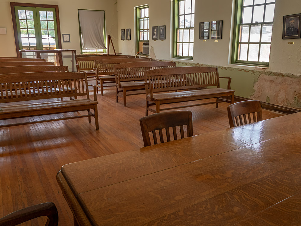 wood benches and table with chairs in old courtroom with windows.