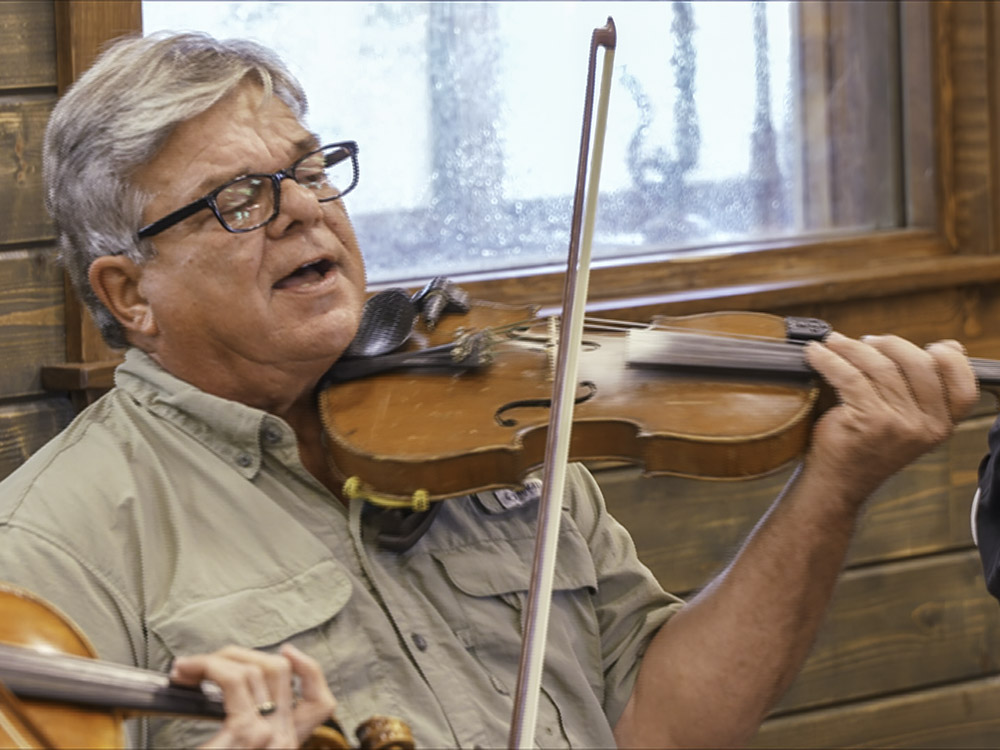man with gray hair, glasses in tan shirt plays fiddle and sings