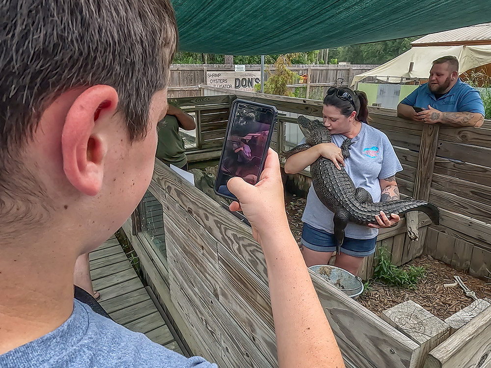 woman in blue shirt poses for selfie photo with alligator.