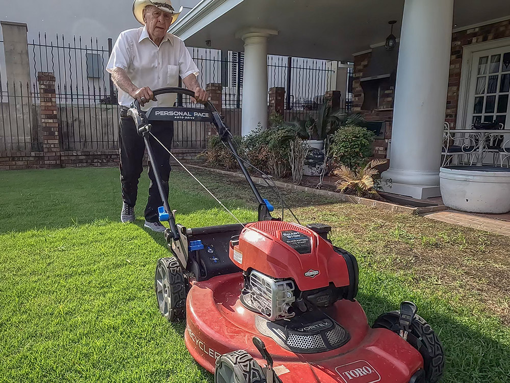 elderly man in white shirt and hat pushing red lawnmower