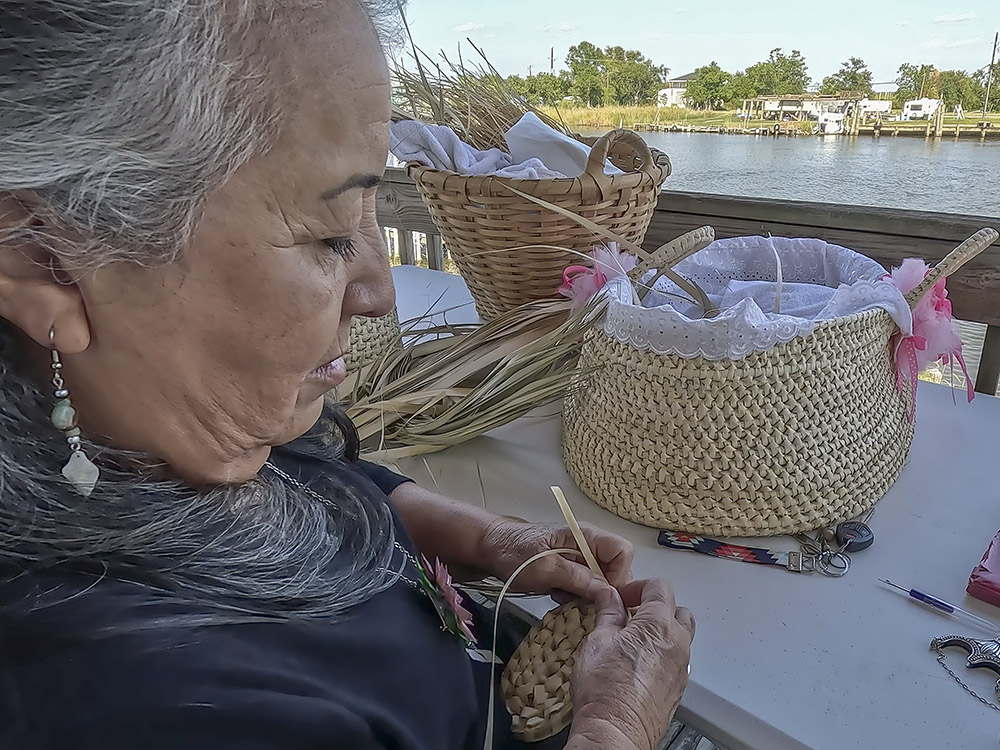 woman with gray hair and dark clothing weaving Houma Indian baskets
